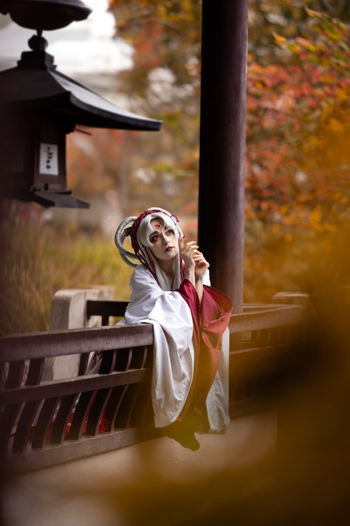 Das Bild zeigt eine Frau in einem japanischen Garten. Sie lehnt an einer Brüstung und schaut in die Ferne
